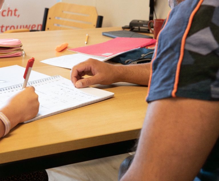 Wiskunde bijles Een hand schrijft in een schrift op een tafel met schoolbenodigdheden.